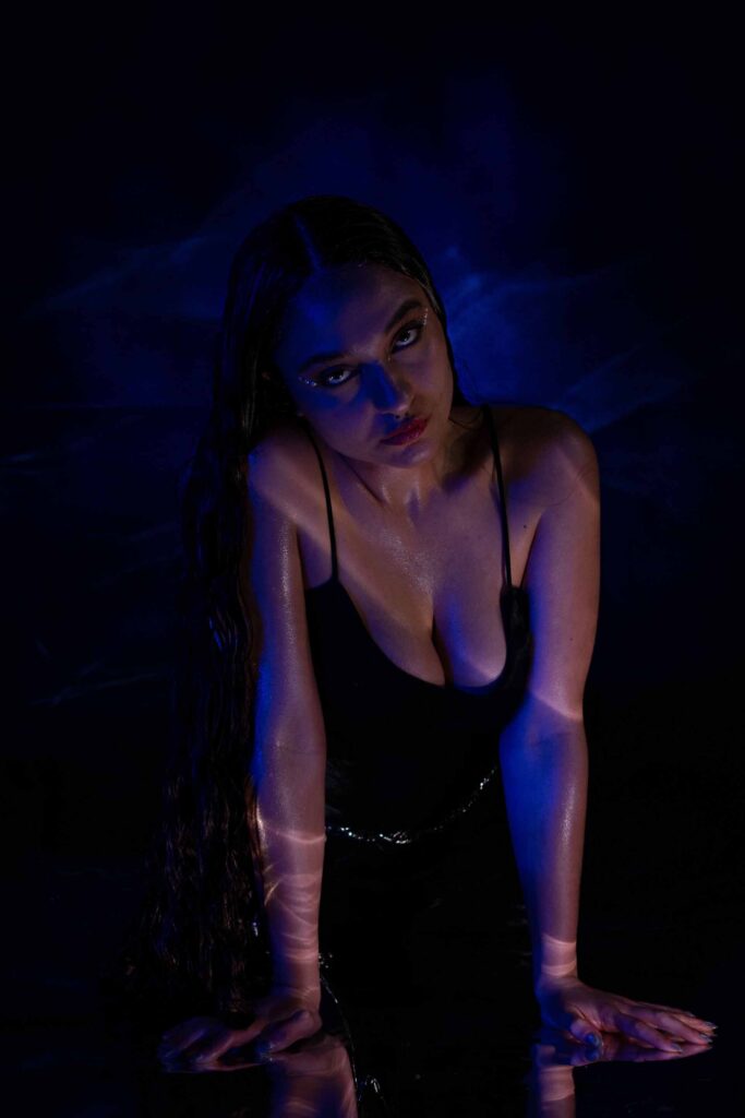 Woman leaning on her arm while laying on floor  in a dark room lit by blue and pink lights