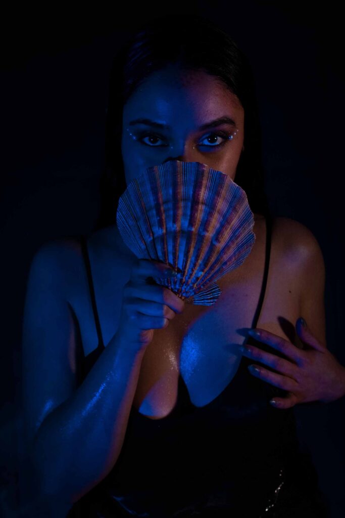 Woman covering half her face with sea shell in a dark room lit by blue and pink lights